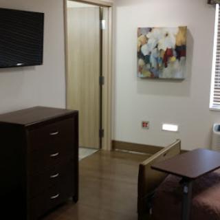 A well-furnished room featuring a cozy bed, a dresser, a wall-mounted TV, and an abstract painting on the wall.