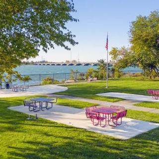 A scenic park by the waterfront with colorful picnic tables and lush green grass on a sunny day.