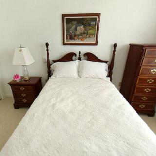 A neatly arranged bedroom with a double bed, nightstand, lamp, and dresser.