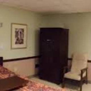 A hotel room with a wardrobe, chair, and wall art.
