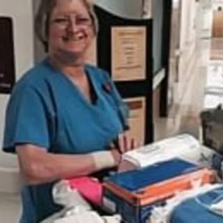 A smiling nurse in scrubs standing by medical equipment in a hospital setting.