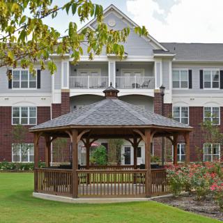 A wooden gazebo in front of a multi-story residential building with a well-maintained garden.