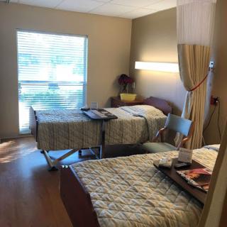 A spacious hospital patient room with two beds and natural light coming through the window.