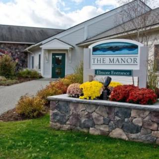 A well-landscaped entrance to The Manor, featuring a sign and colorful flowers.