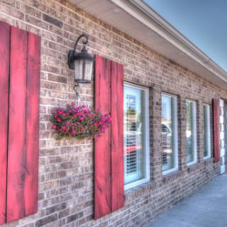 A charming brick building featuring red shutters, decorative flowers, and a classic lantern.