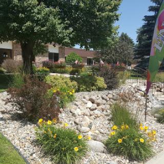 A beautifully landscaped garden featuring vibrant flowers and natural stone formations, surrounded by lush greenery on a sunny day.