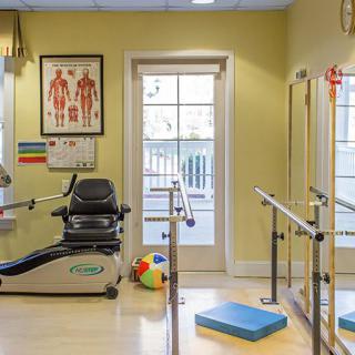 A well-lit physical therapy room equipped with exercise machines and training tools.