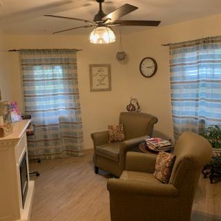 A cozy living room with armchairs, a fireplace, and a ceiling fan.