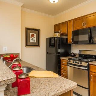 A modern kitchen with wood cabinets and a granite countertop, featuring appliances like a refrigerator, stove, and microwave.