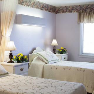 A cozy bedroom with twin beds, decorated with lamps and flowers on nightstands.