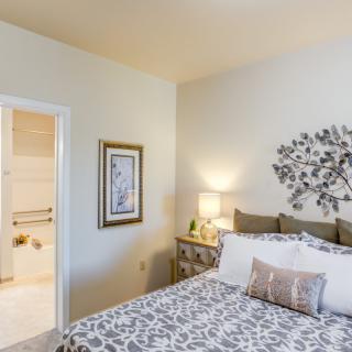 A cozy bedroom featuring a bed with patterned bedding, a nightstand with a lamp, and decorative artwork on the wall.