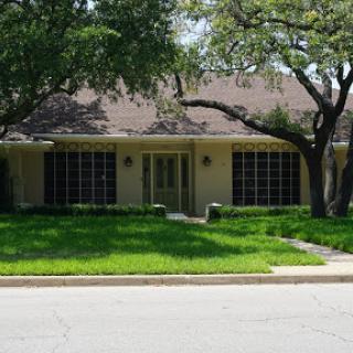 A charming single-story house surrounded by lush green grass and mature trees.