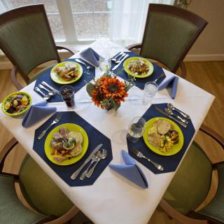 A beautifully arranged dining table set for four, complete with a floral centerpiece, neatly folded napkins, and prepared meals on colorful plates.