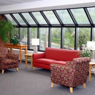 A cozy lounge area with a red sofa, patterned chairs, and large windows overlooking greenery.