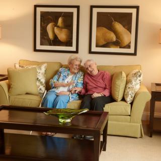 An elderly couple smiling while sitting on a couch in a cozy living room.