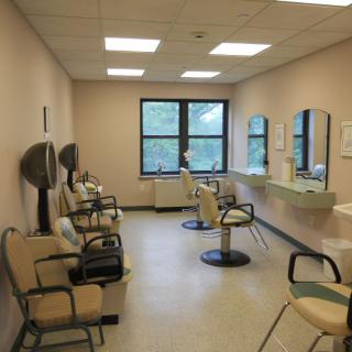 An empty hair salon with chairs facing mirrors and large windows.