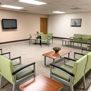A modern and inviting waiting room with green chairs and wooden tables.