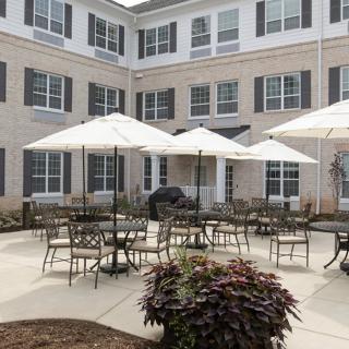 A spacious outdoor patio area with tables, chairs, and umbrellas in front of a multi-story building.