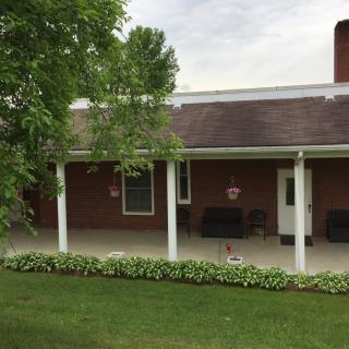 A brick house with a covered patio and a well-maintained lawn.