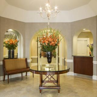An elegantly decorated lobby featuring a central table with flowers and a chandelier above.