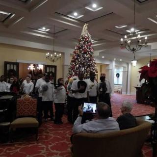 A group of people posing for a photo in front of a large Christmas tree inside a festive room.