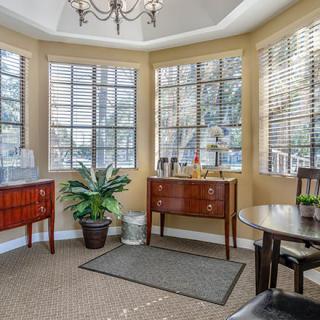 A cozy living room with large windows, wooden furniture, and a potted plant.