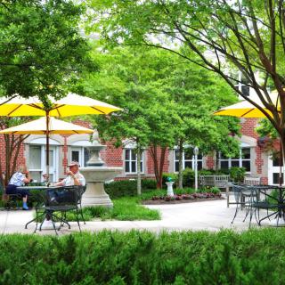 A peaceful outdoor patio area with tables, chairs, and yellow umbrellas surrounded by lush greenery.