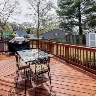 A wooden deck in a backyard featuring a glass table with chairs and a grill.