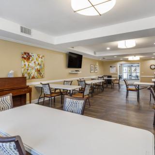 A spacious dining area with multiple tables and chairs, featuring a piano and a mounted television on the wall.