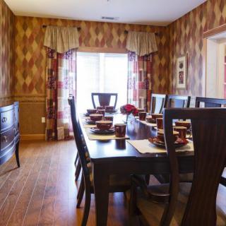 A warmly decorated dining room featuring a large wooden table and chairs, with elegant wallpaper and curtains.