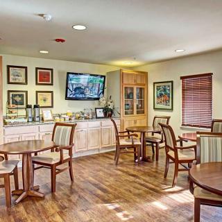A cozy indoor seating area with wooden floors, several tables and chairs, decorated walls, and a television.
