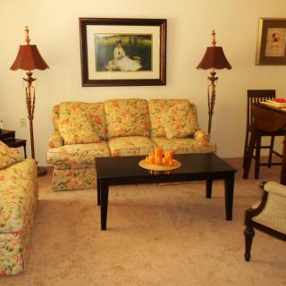 A cozy living room featuring floral upholstered sofas, a black coffee table with decorative fruit, and warm lighting from two lamps.