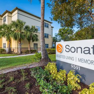 A sunny day view of Sonata building with a sign in the foreground surrounded by lush landscaping and palm trees.