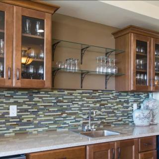 Modern kitchen with wooden cabinets, glass shelves, and a colorful tile backsplash.