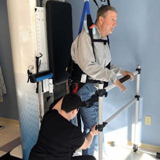 A patient is assisted in a walking rehabilitation device during a physical therapy session.