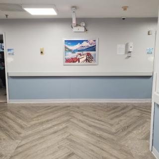 A view of a hospital corridor featuring an artwork on the wall and a patterned floor.