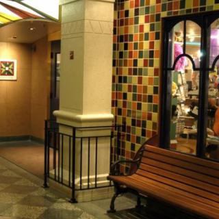 A cozy seating area inside a shopping mall, featuring a wooden bench next to a storefront with colorful tiled walls.
