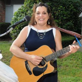 A woman playing the guitar and singing outdoors.