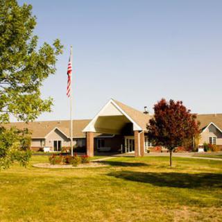 A building with an entrance, surrounded by trees and grass, with a flagpole in front.