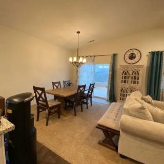 A cozy dining and living area with a wooden table, chairs, and a comfortable couch, accented by a chandelier and decorative curtains.