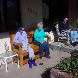 Three elderly individuals sitting outdoors on a patio enjoying the sunshine.