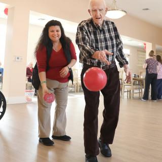 An elderly man enjoying a game of indoor bowling with assistance.