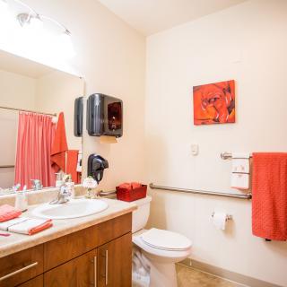 A bright bathroom featuring orange accents with a sink, toilet, and mirror.