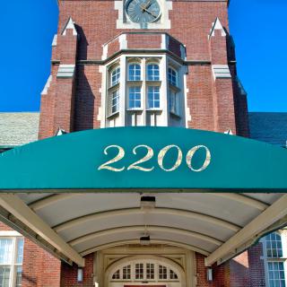 A brick building with a green awning displaying the number 2200, featuring an ornate entrance and a clock tower.