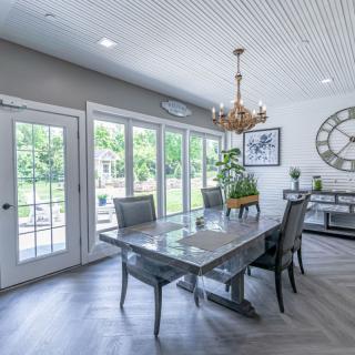A modern dining room with a large table, stylish chairs, and a chandelier, featuring ample natural light through French doors.