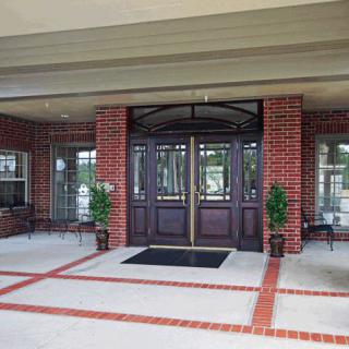 The entrance of a brick building with double doors and potted plants on either side.