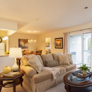 A cozy living room with a beige sofa, coffee table, and dining area in the background.