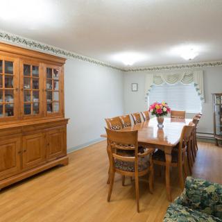 A spacious dining room with a long wooden table and matching chairs, alongside a large wooden cabinet.