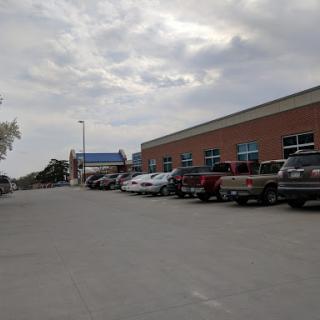A view of a busy parking lot next to a commercial building under a cloudy sky.