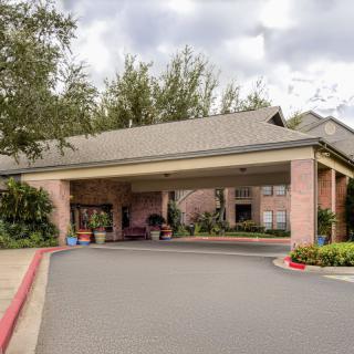 A building entrance with a covered driveway surrounded by trees and landscaping on a cloudy day.
